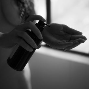 Women's Circle Balancing Body Oil III bottle in a woman's hand by a window