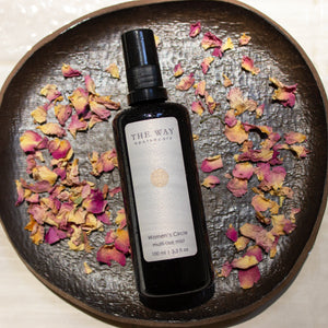 Women’s Circle Multi-Use Mist bottle on a plate of rose petals—aromatherapy mist with rose otto for hormonal balance, mood support, and skin hydration.