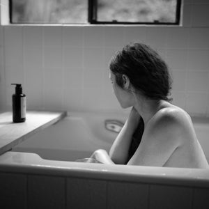 Women's Circle Balancing Body Oil II on a tray with a woman in a bath